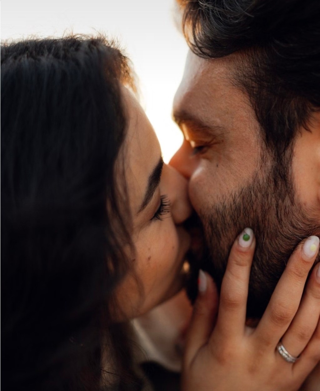Casal se beijando em close, com a mão dela apoiada no rosto dele