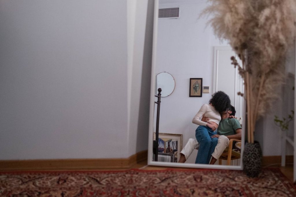 Casal se beijando diante do reflexo de um espelho em um quarto intimista.