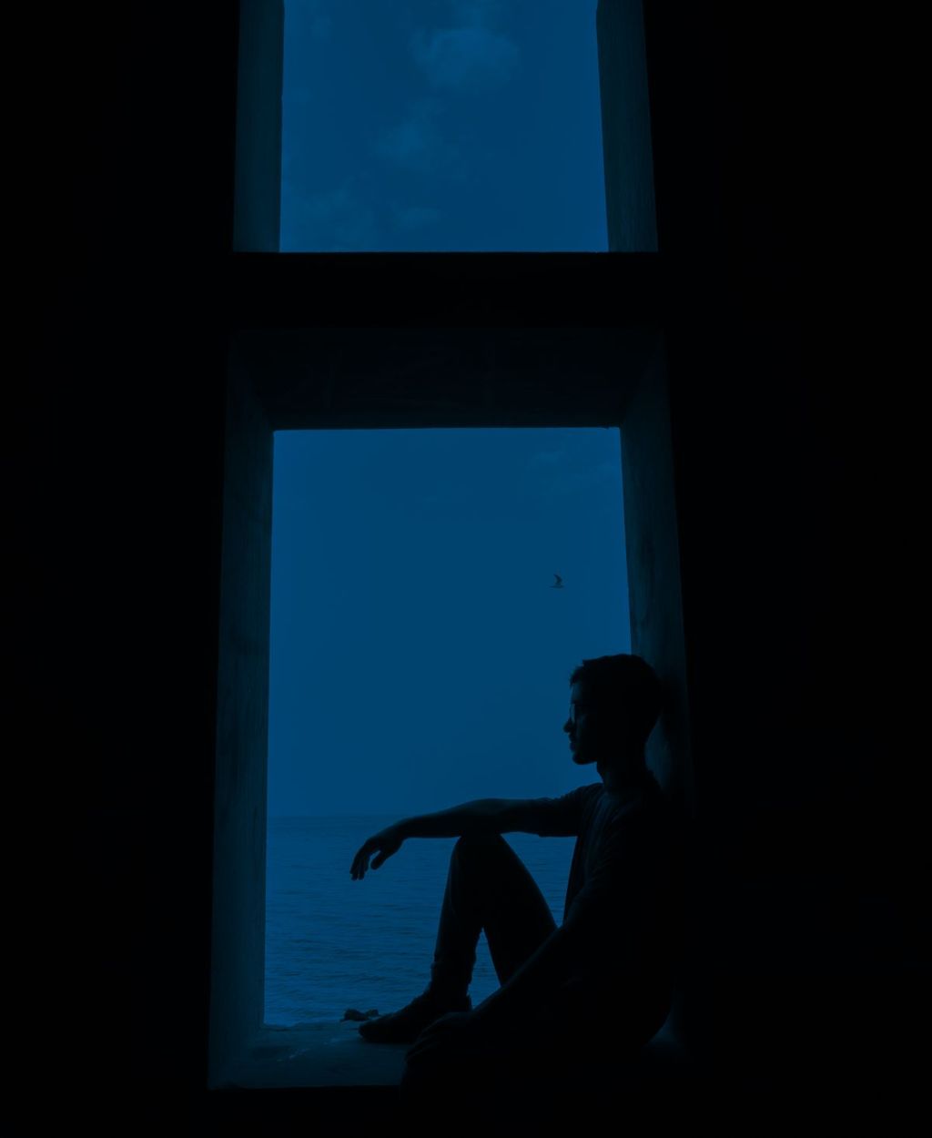 Silhueta de uma pessoa sentada diante da janela, envolvida pelo azul escuro da noite.